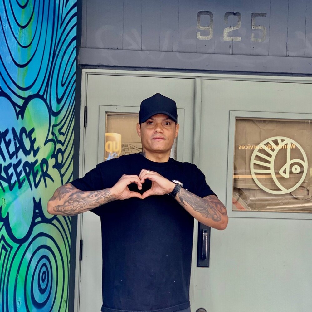 Jamal Blake-Williams in front of his business making a heart sign with his hands