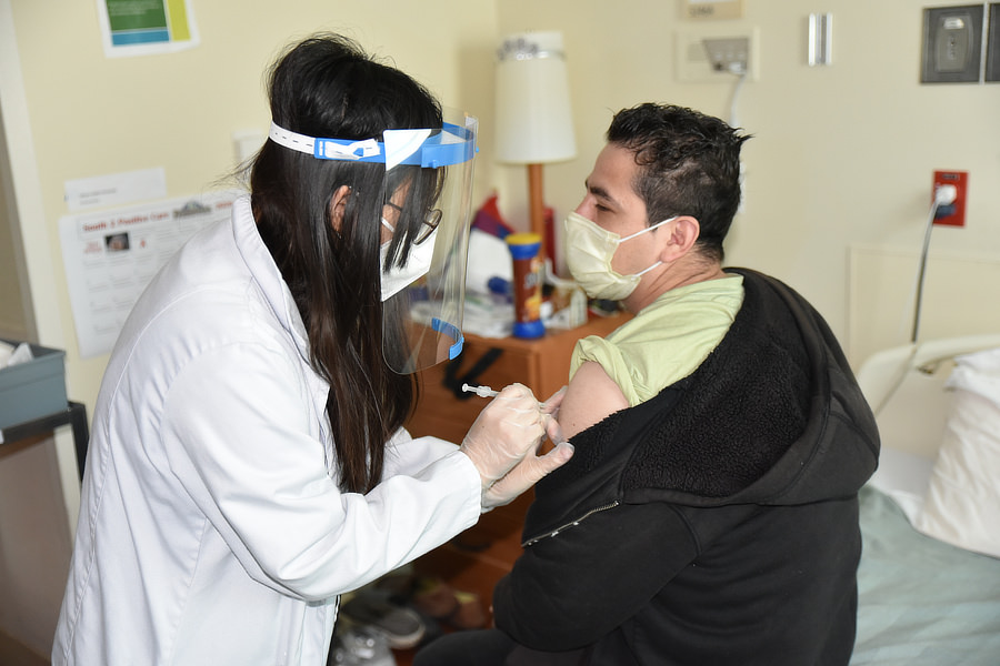 A nurse wearing PPE gives Hilario a shot.