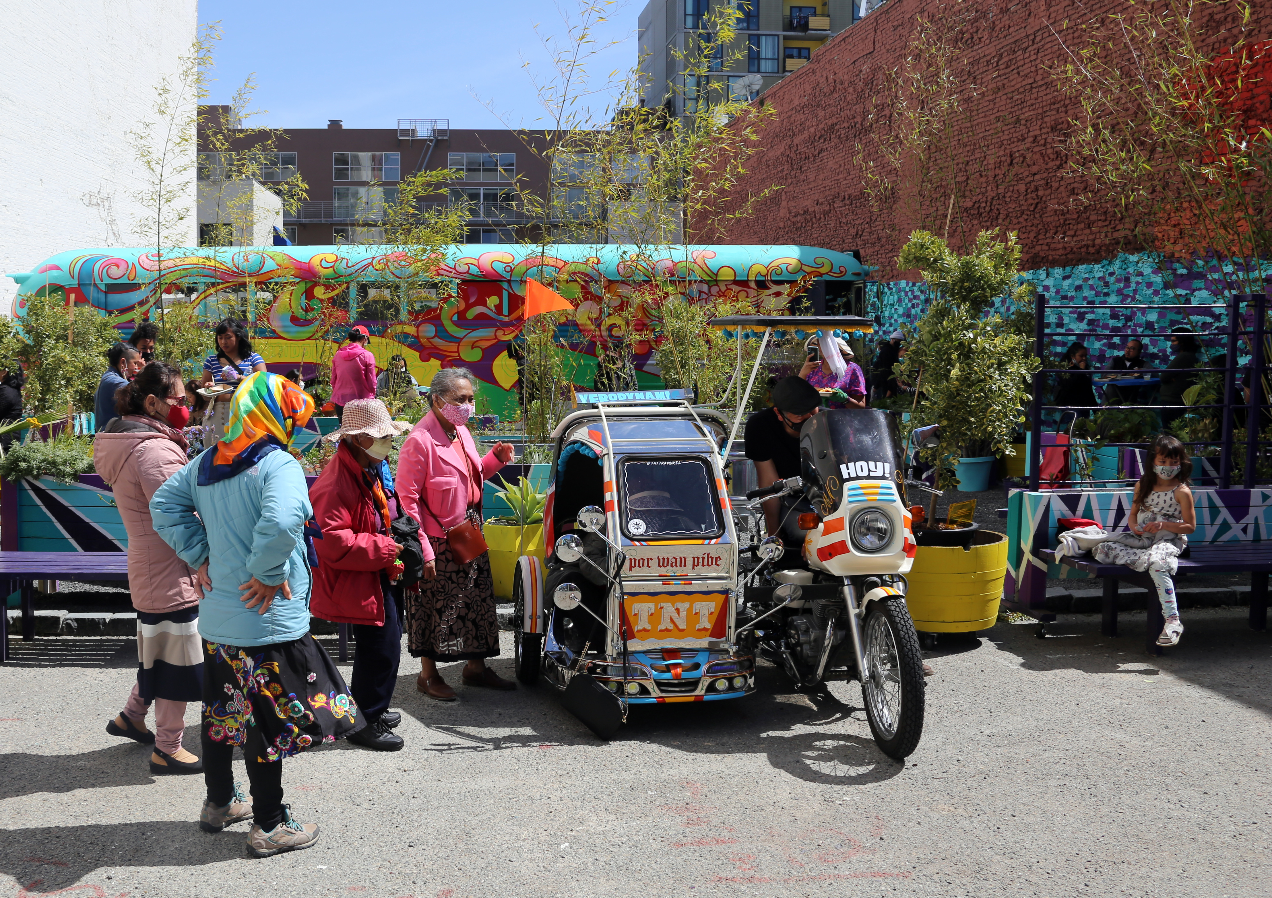 5 people standing outside in a colorful garden with a motorbike and bus