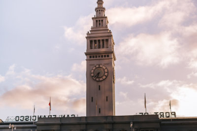 View of the Ferry Building from the street, with soft clouds in the background. "Port of San Francisco" can be seen backward at the lower edge.