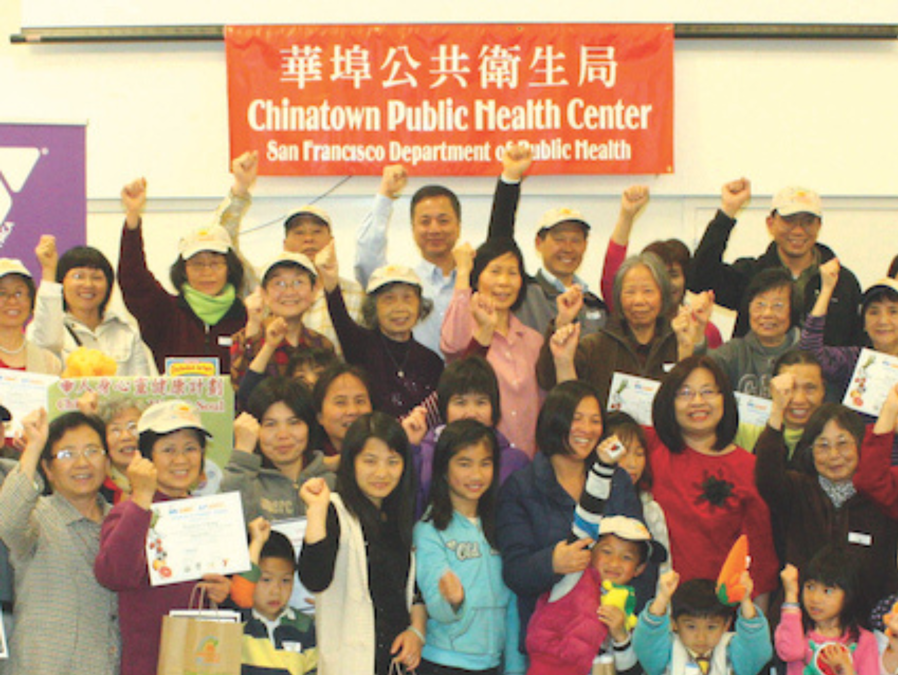 Group of adults and children in a nutrition program cheer for the camera 