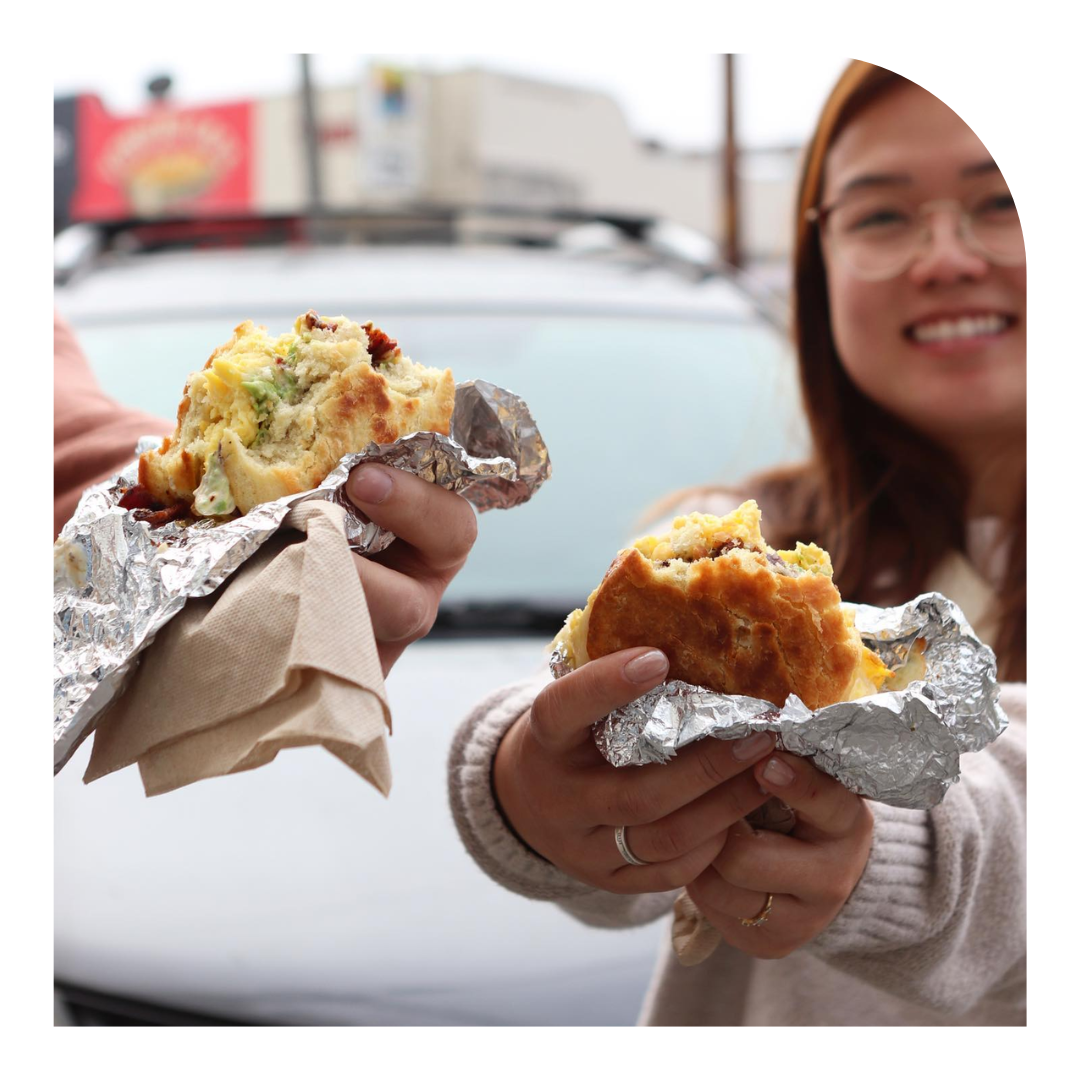 photo of two people holding their breakfast sandwiches towards the camera