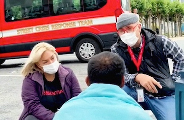 Two masked outreach workers talking to a potential client with the Street Crisis Response van behind them