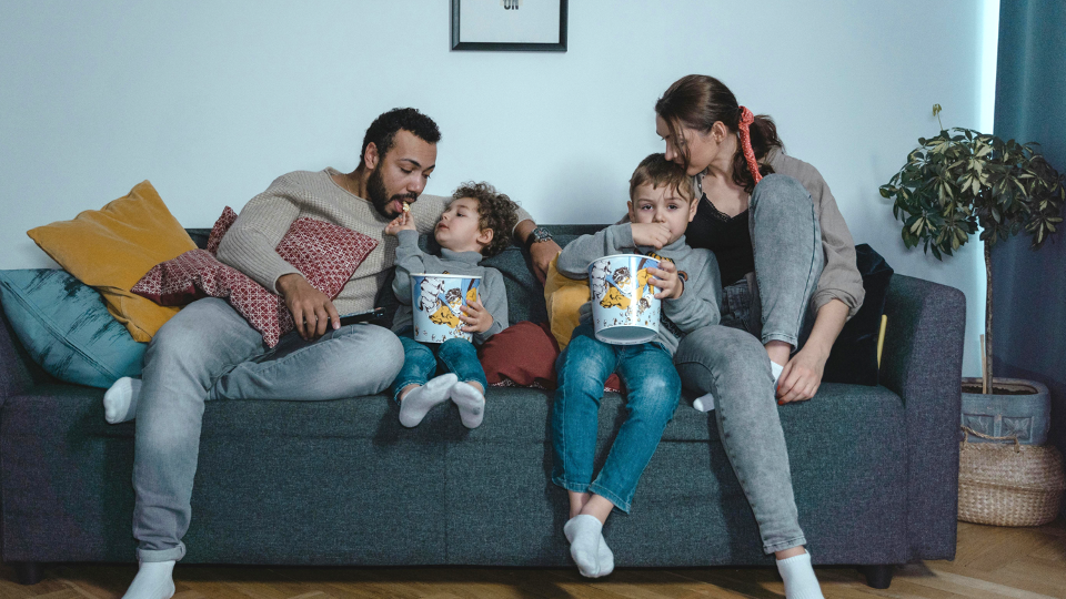 Family sitting on blue sofa eating popcorn.