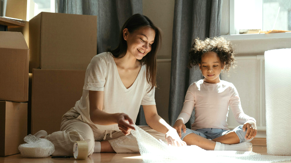 A mother and a daughter sit on the ground packing home items.