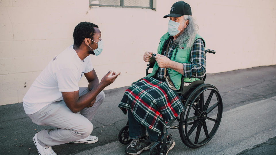 A volunteer speaks to a man in a wheelchair. 