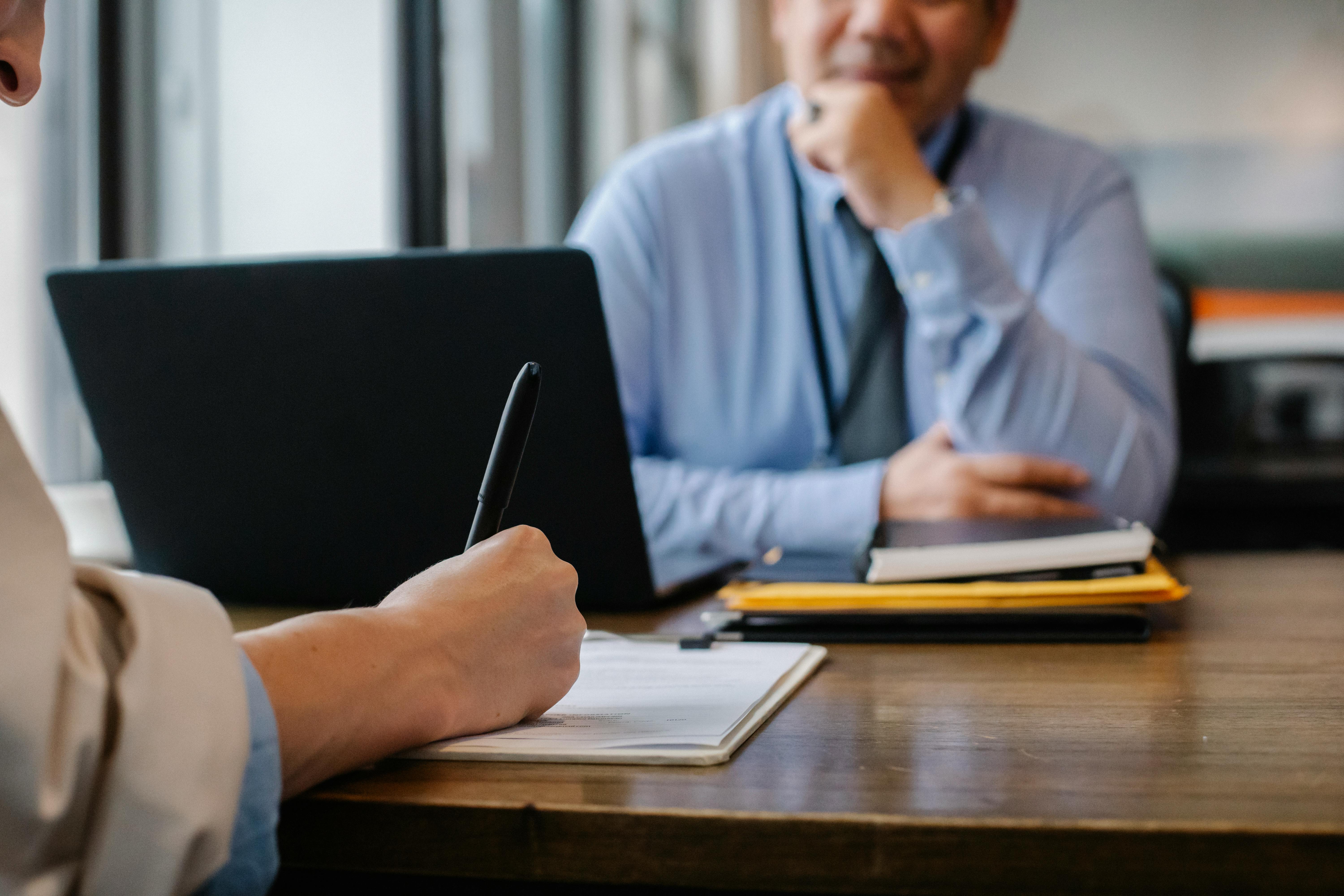 two people sitting at a table while one writes on paper