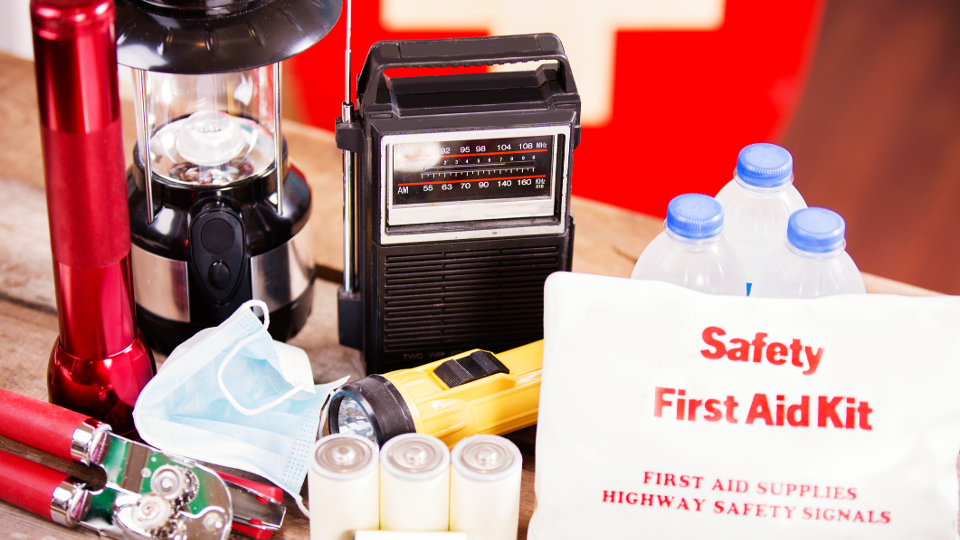 Natural disaster supplies (hurricane, flood, earthquake, etc.): flashlight, batteries, water bottles, first aid kit, lantern, radio, mask. No people.