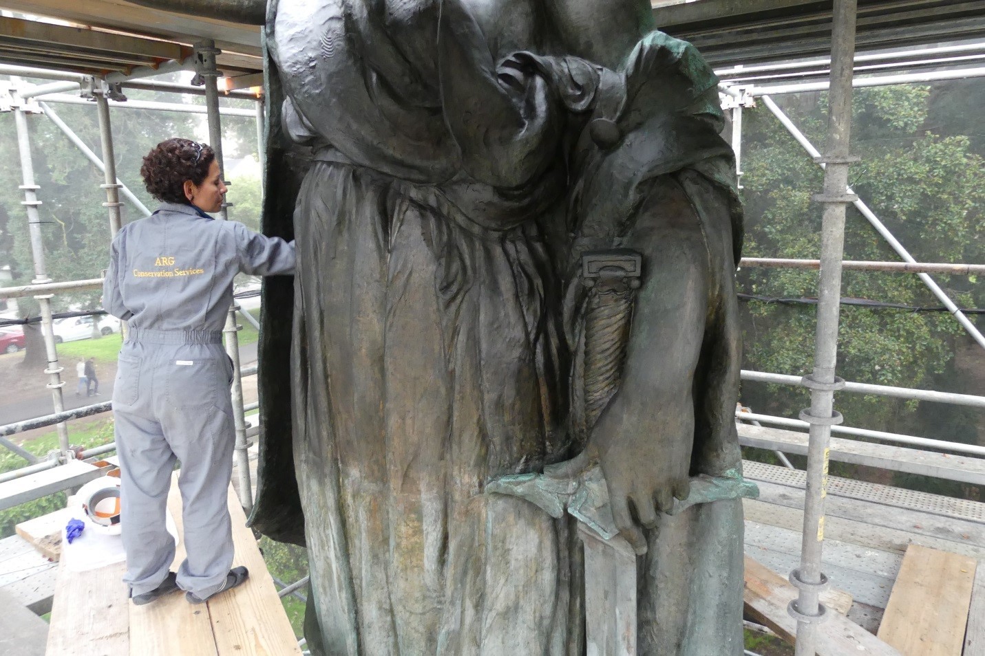 Image of fine arts conservator cleaning and applying a protective wax coating to the 5-story tall bronze sculpture.