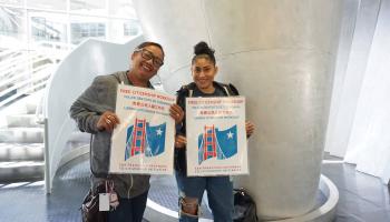 Two smiling people hold a sign for the citizenship workshop 