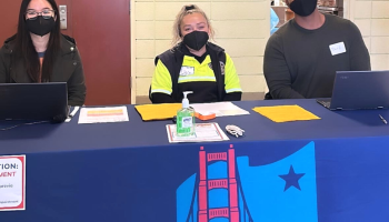 Three people wearing face masks sit a the registration table for a San Francisco Pathways to Citizenship workshop