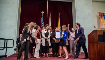 A group celebrates receiving the Immigrant Leadership Award on stage at City Hall
