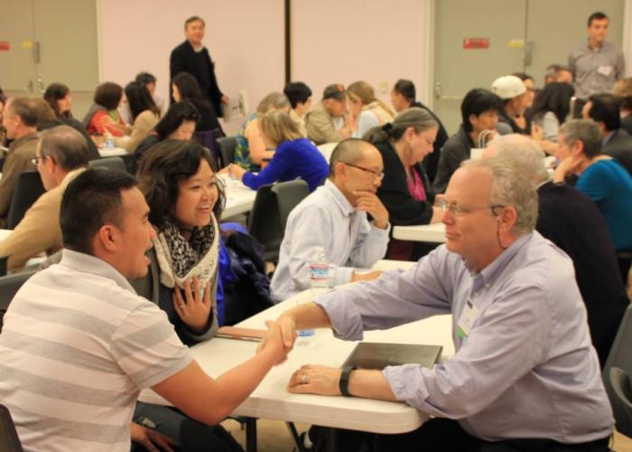 A couple talks to a financial planner in a room full of similar meetings