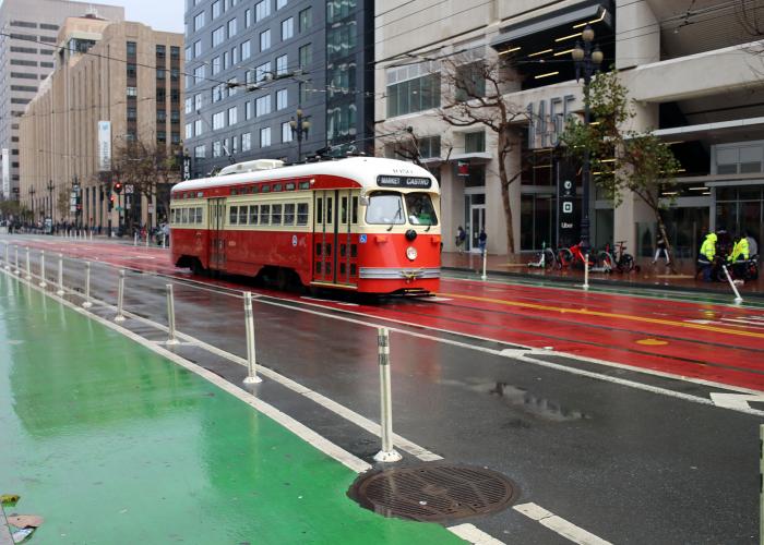 A red and beige trolley drives down a wet San Francisco street