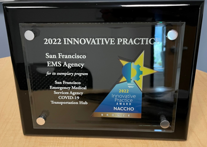 Rectangular shaped, black plaque with a glass front. The plaque contains the words "2022 Innovative Practice San Francisco EMS Agency for its exemplary program San Francisco Emergency Medical Services Agency COVID-19 Transportation Hub, 2022 NACCHO Innovative Practice Award Bronze