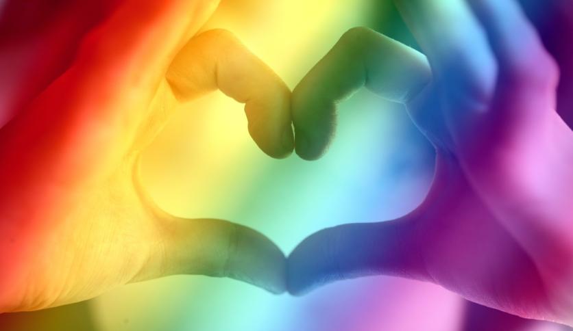Two hands making a heart in rainbow light