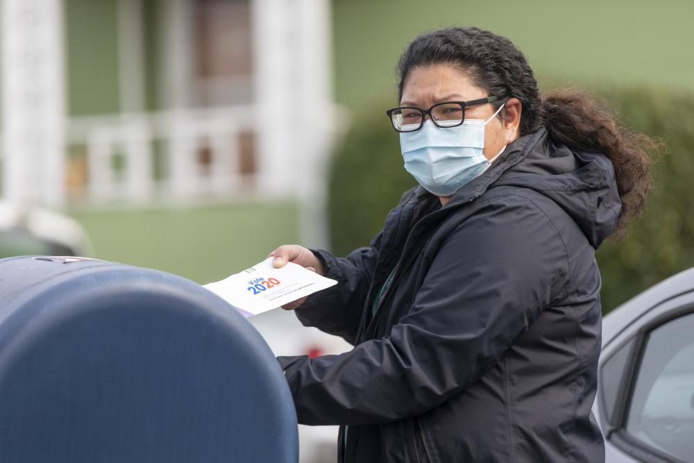 Woman in face mask puts her election ballot in mailbox