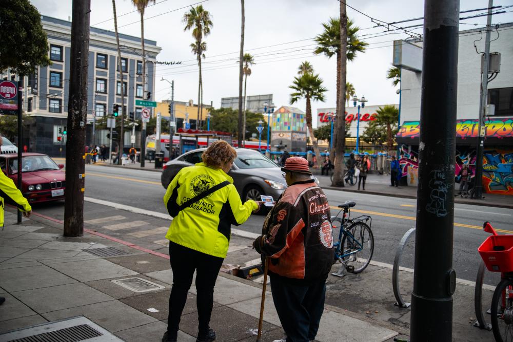 A Community Ambassador shows a resident a flyer on 16th and Mission Streets