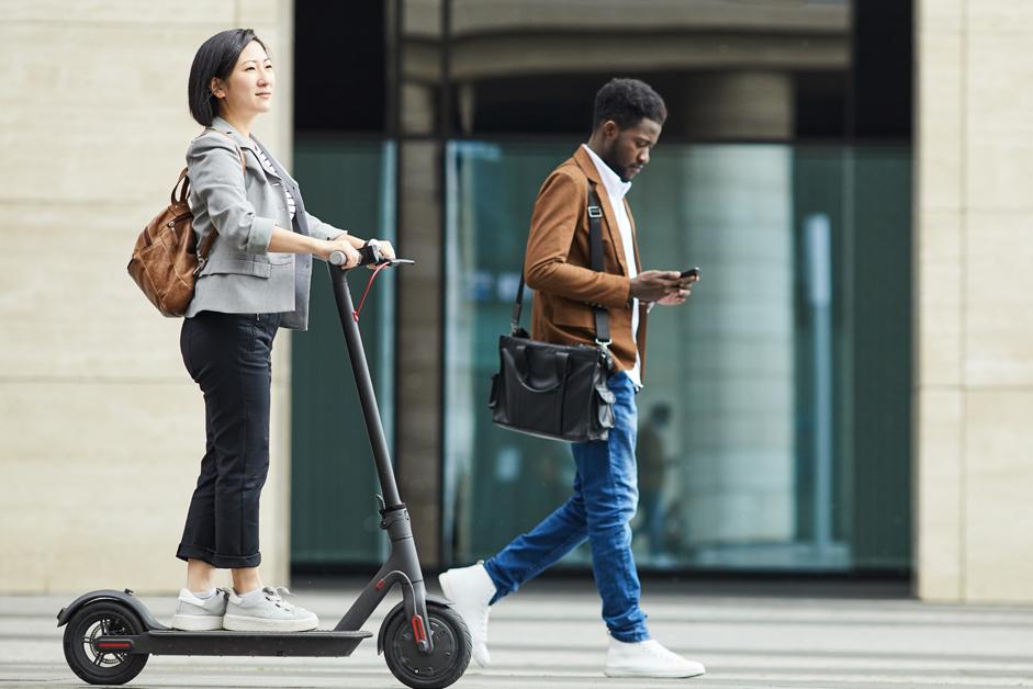 Woman riding a scooter next to a man looking at his phone