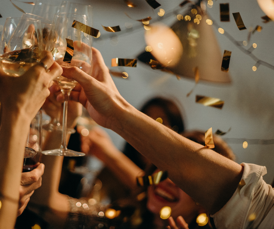 several hands holding glasses and toasting, with gold confetti in the air