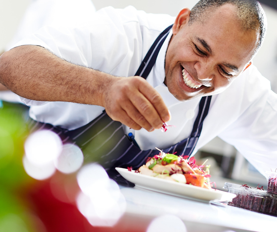 person smiling while garnishing a plate of food