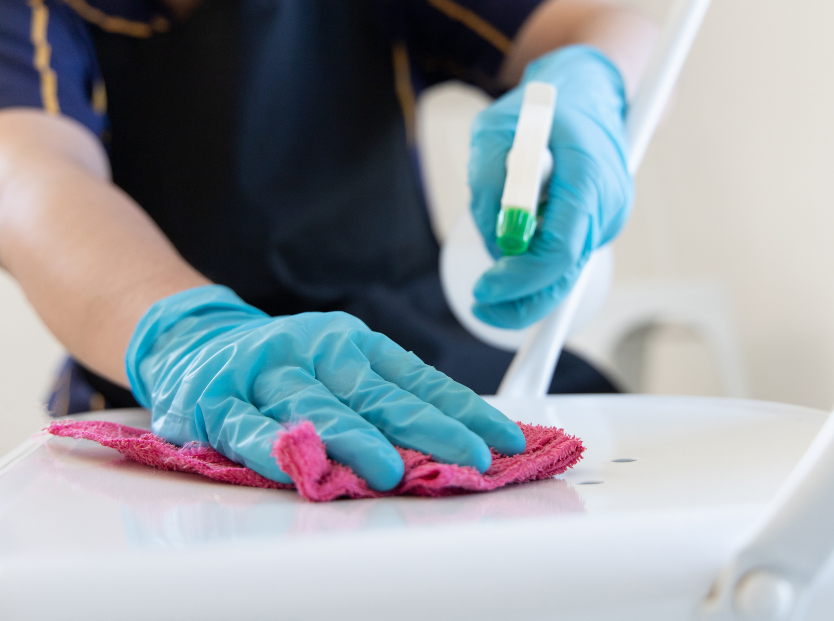 photo of hands in teal rubber gloves, spraying cleaner and wiping with a pink cloth