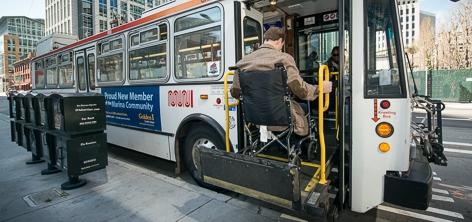 Man in wheelchair uses mechanical lift to get on SF Muni bus. 