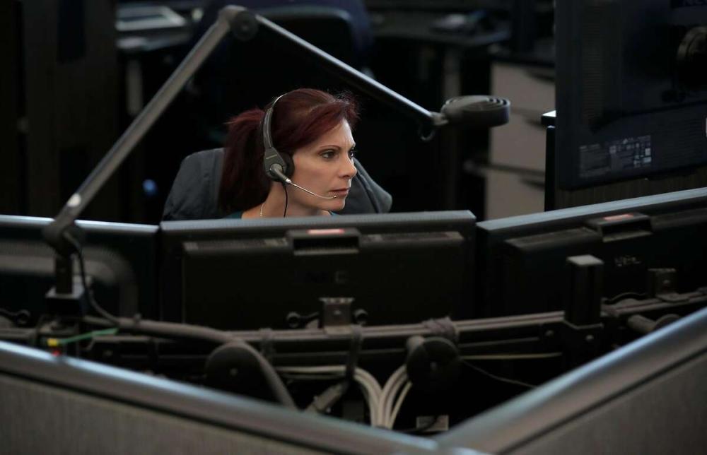 Picture show a woman sitting in from of multiple computer screens wearing a headset.