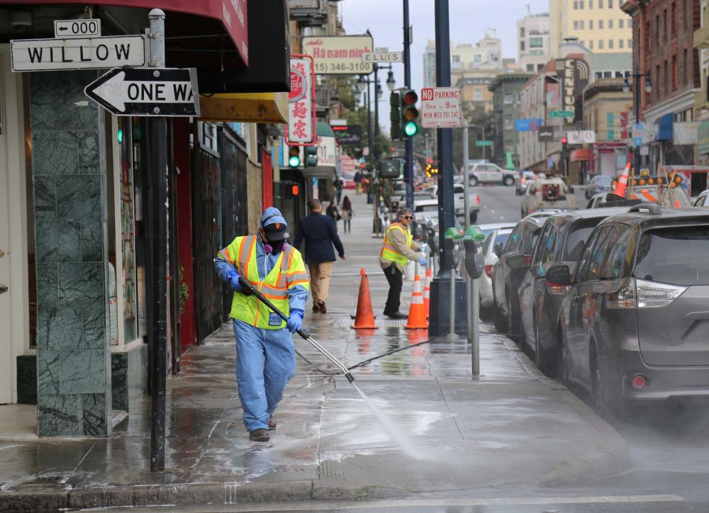 Public Works street cleaner wearing safety equipment power washing a sidewalk in Chinatown.