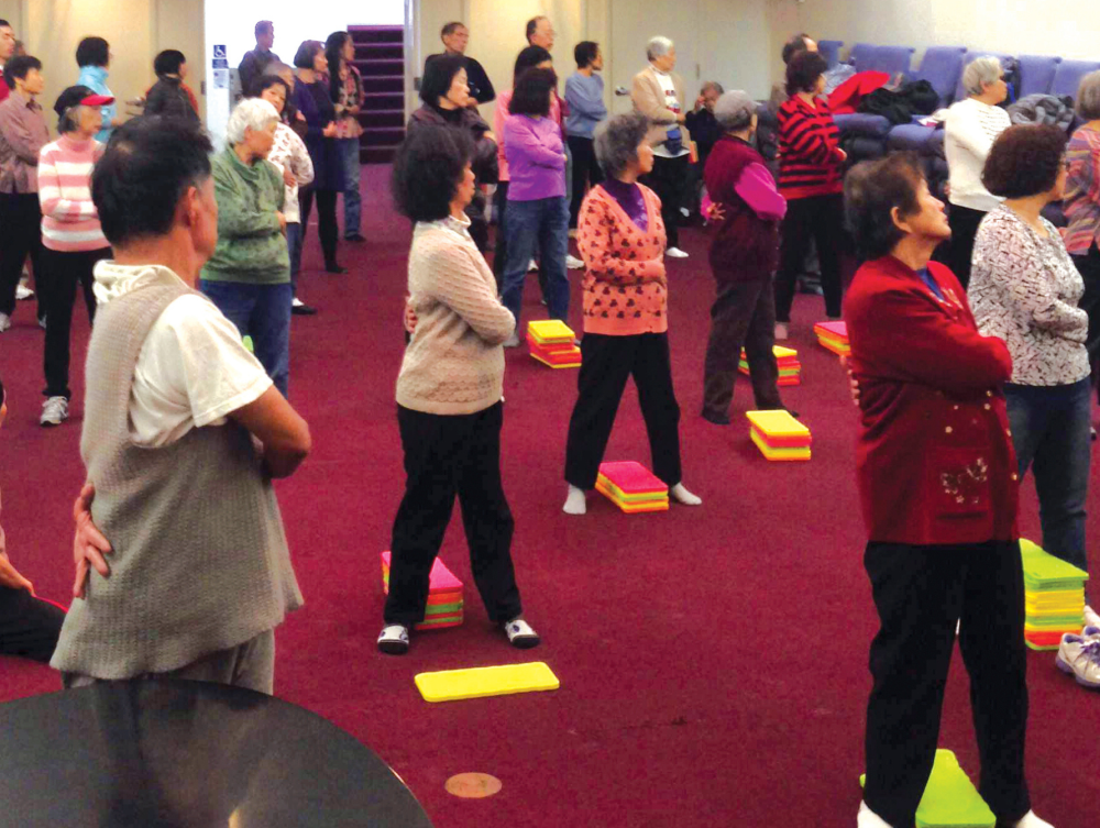 A group of people doing gentle exercise movement in a recreation room.
