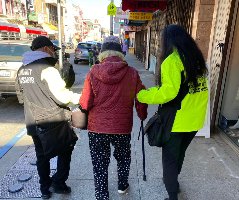 Two Community Ambassadors help an elderly person walk down the street