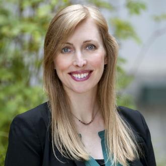 Woman with long blonde hair wearing a black jacket and teal green top.