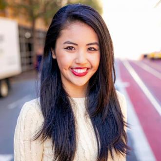 Photo of Commissioner Sharon Chung, who has dark hair, is wearing a white long sleeve top and red lipstick and is smiling