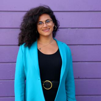 Shane Zaldivar from office of transgender initiatives smiling to the camera in a blue blazer and black shirt in front of purple background