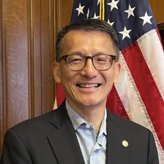 Commissioner Leung is a middle aged man standing in front of the US flag