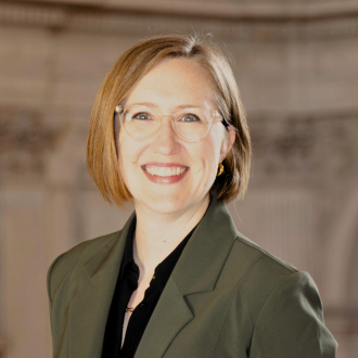 photo of woman wearing olive green jacket with short, dark blond hair and glasses